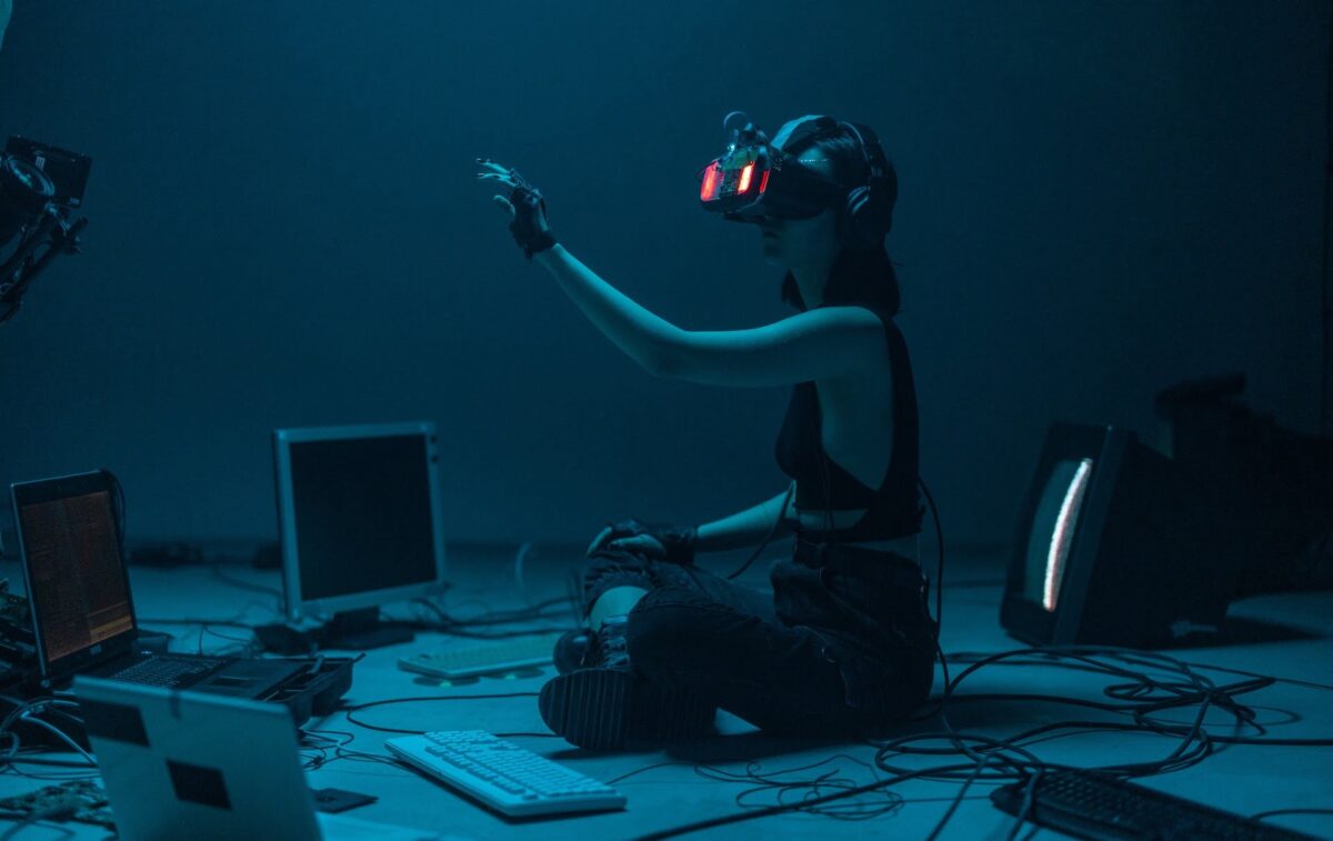 Young woman with VR glasses sits on floor surrounded by computer and interacts with hand in virtual world