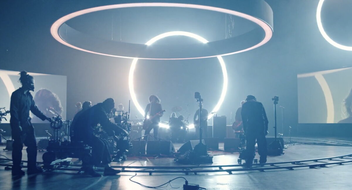 Foo Fighters play a concert surrounded by light rings and a camera crew.