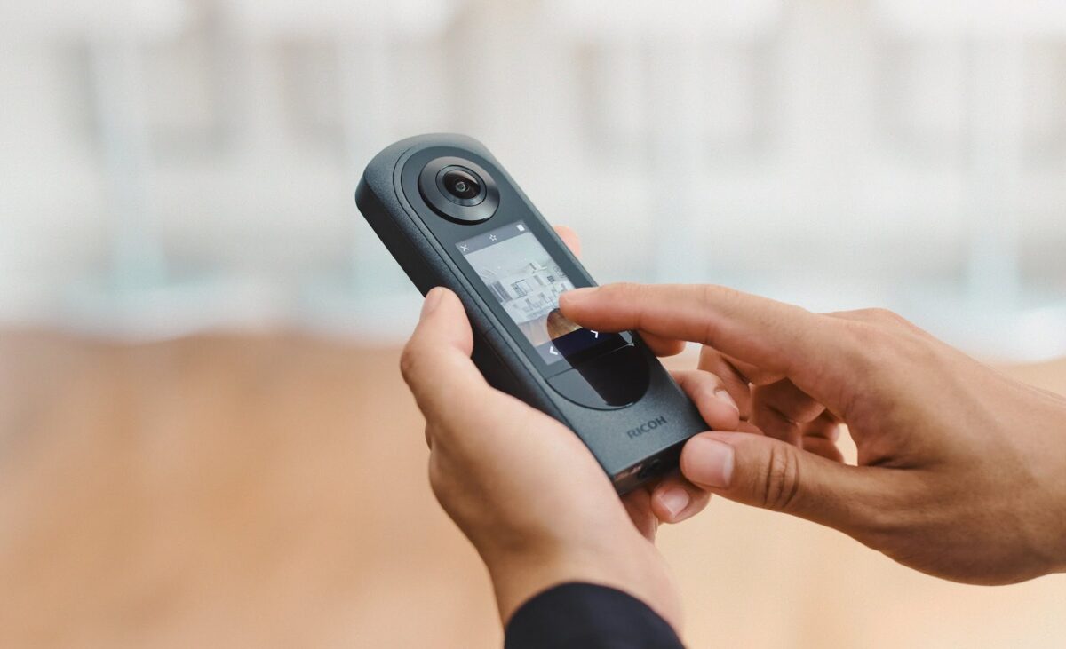 The Ricoh Theta X VR camera in the hands of a user.