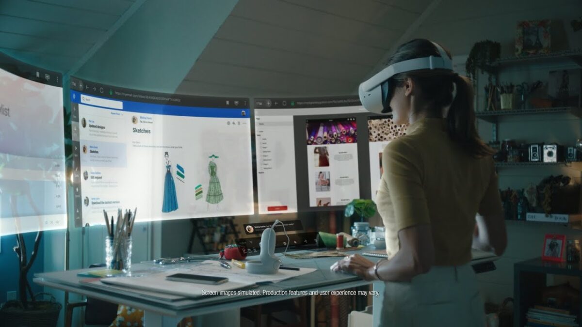 A woman with Oculus Quest VR goggles on her head stands at a desk and looks at digital screens.