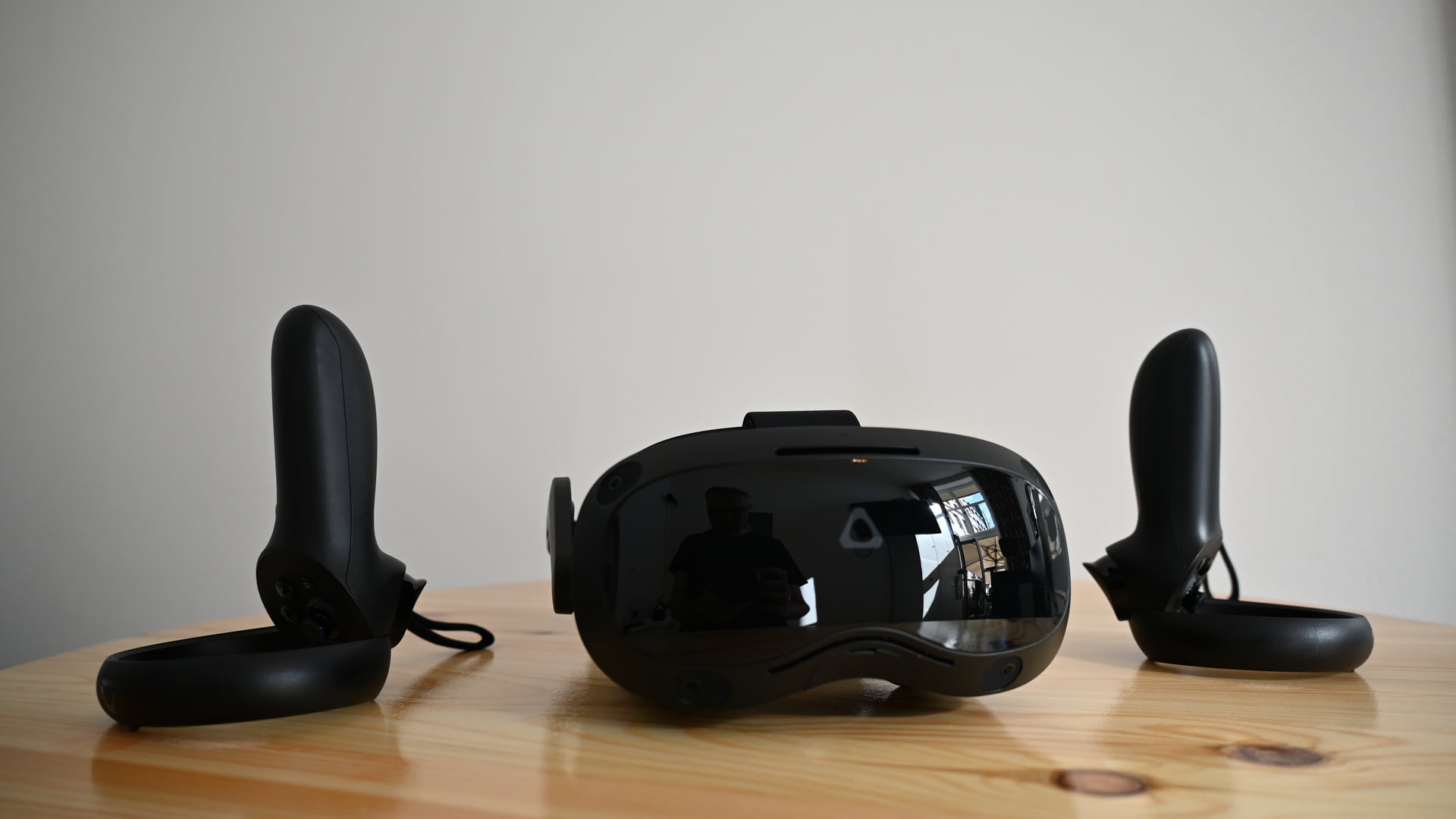 Black VR headset Vive Focus 3 from front on table, flanked by two VR controllers