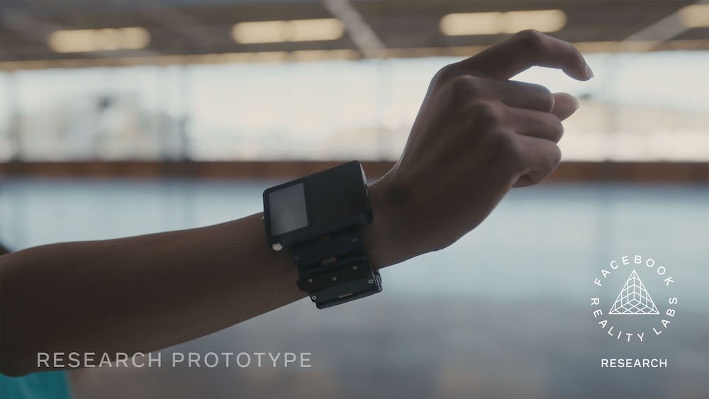 Eine Hand trägt Metas EMG-Armbandprototyp und macht eine subtile Geste in der Luft.