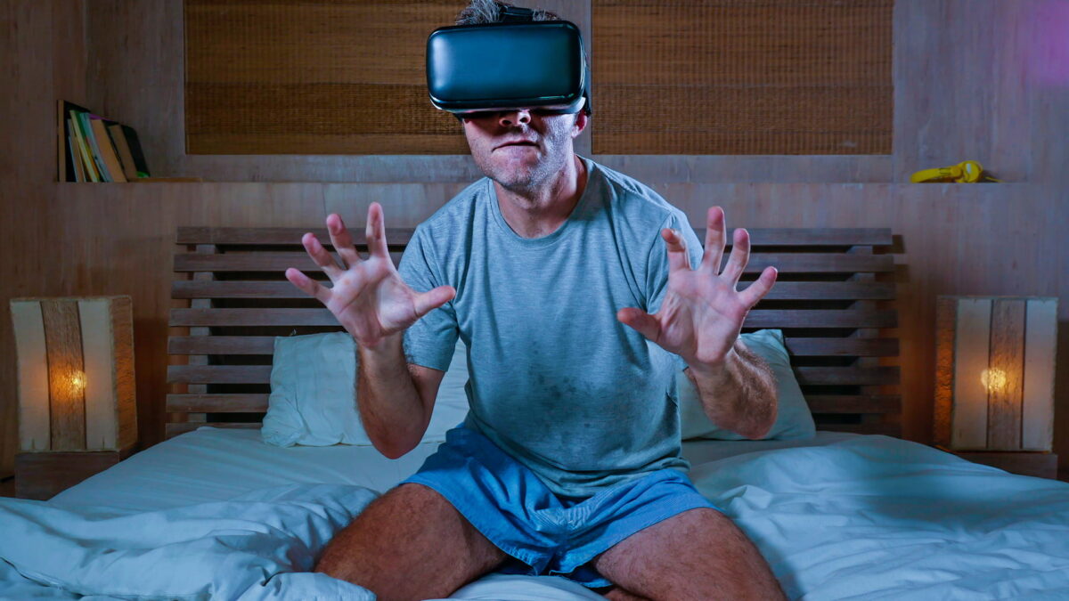 Man on bed with VR headset apparently watching VR porn