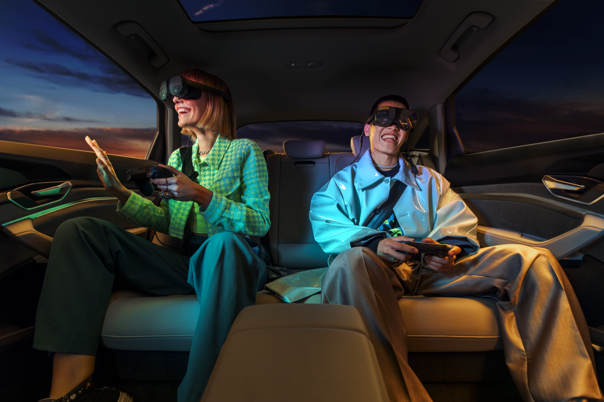 A woman and a man in the back seat of a car are happily grinning as they use the Holoride car VR system.