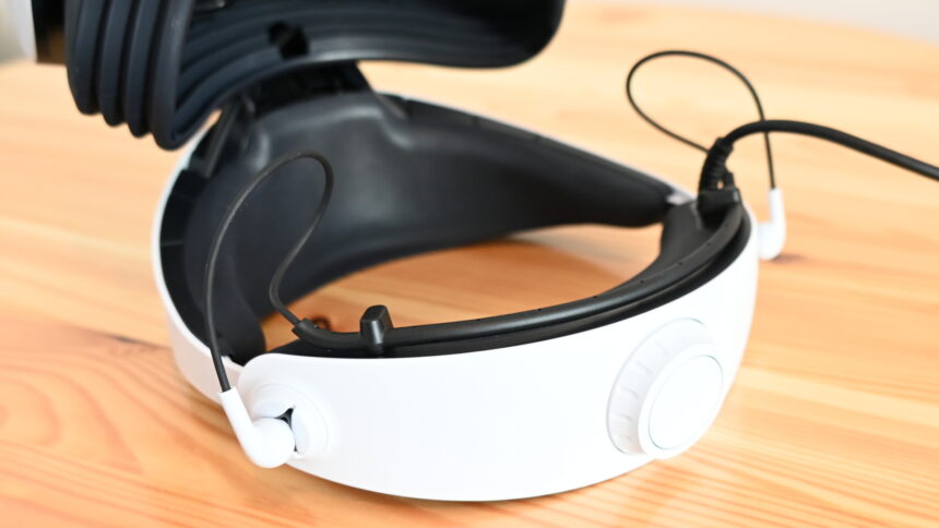 The in-ear earphones of the Playstation VR 2 directly at the rear halo area of the VR headset, which lies upside down on a table