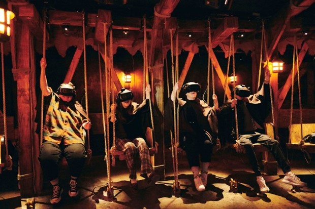 Four people sitting on swings with a VR headset on.