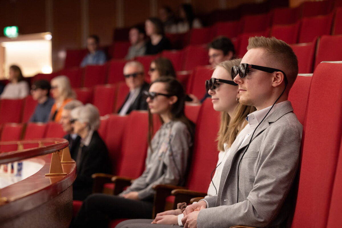 Women and men wearing AR headsets sit in the auditorium of an opera house.