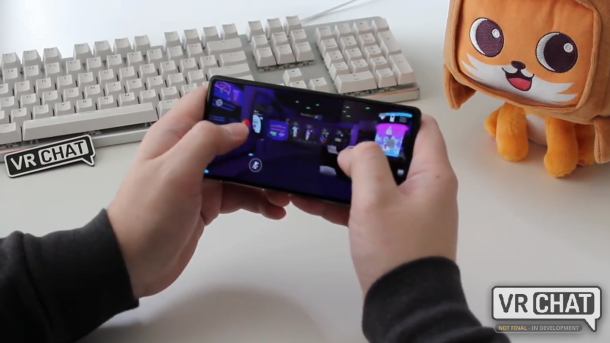 Two hands operate VRChat on an Android smartphone, next to a plush cat and a keyboard.