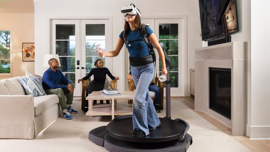 A woman uses the Virtuix treadmill in the living room.  In the background, friends follow the VR action on a TV.