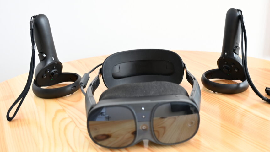 The Vive XR Elite VR headset from the front on a table, with the Vive Focus 3 controllers behind it on the right and left.