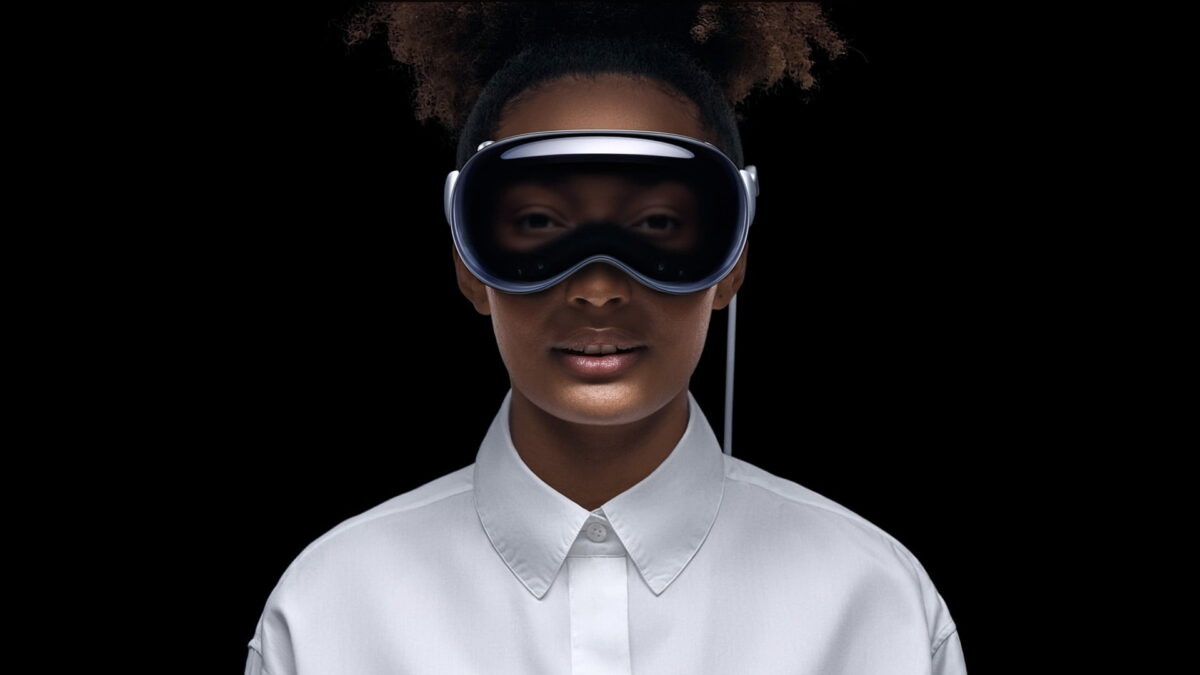 Woman wearing Apple Vision Pro against black background. Her eyes shine through the surface of the headset.
