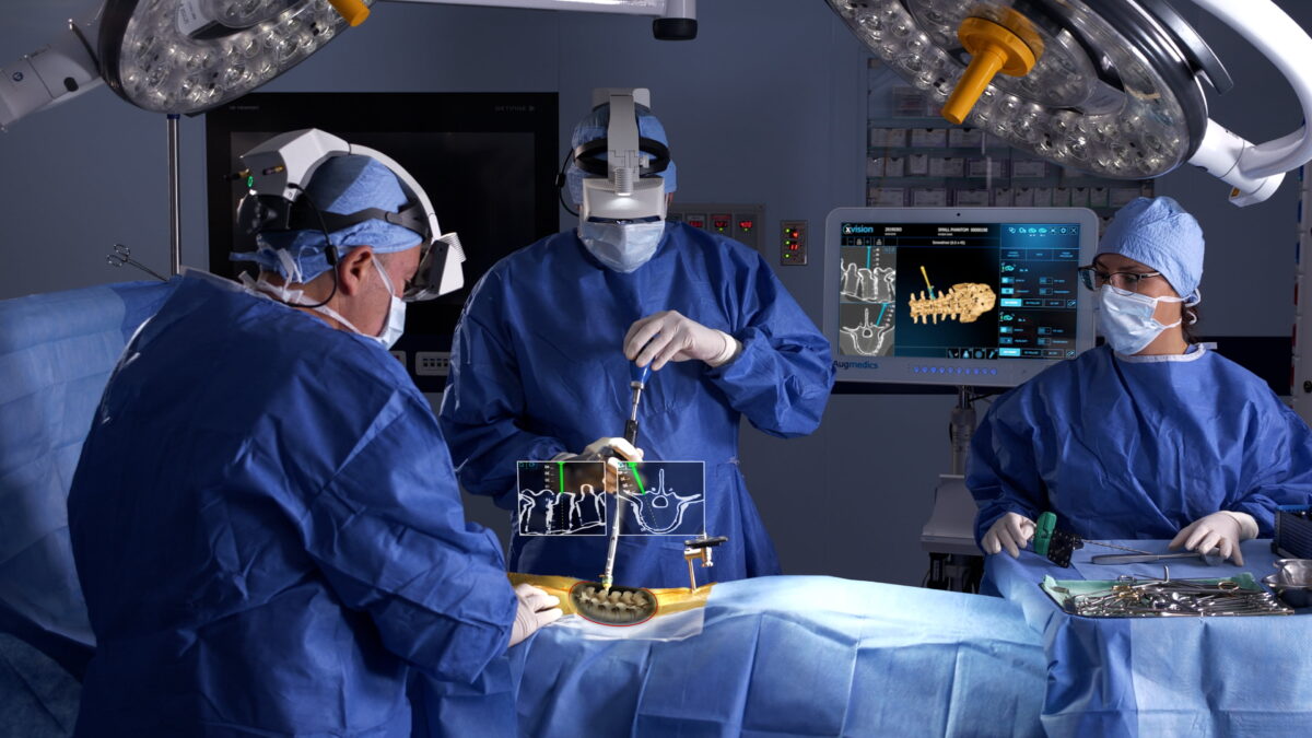 Two surgeons and a surgical assistant in an operating room. The surgeons have AR headset on.