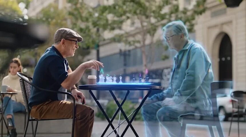A man plays chess outside with a friend, who appears as a hologram.