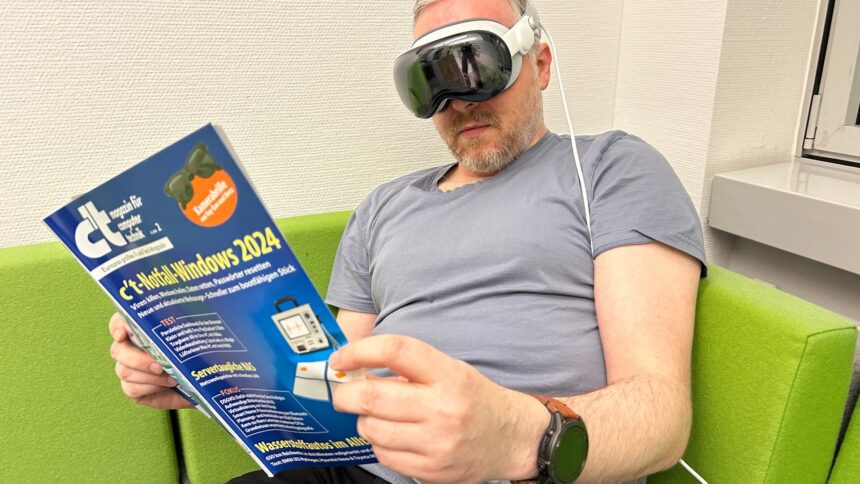 Man with c't magazine in hand on the couch while wearing an Apple Vision Pro