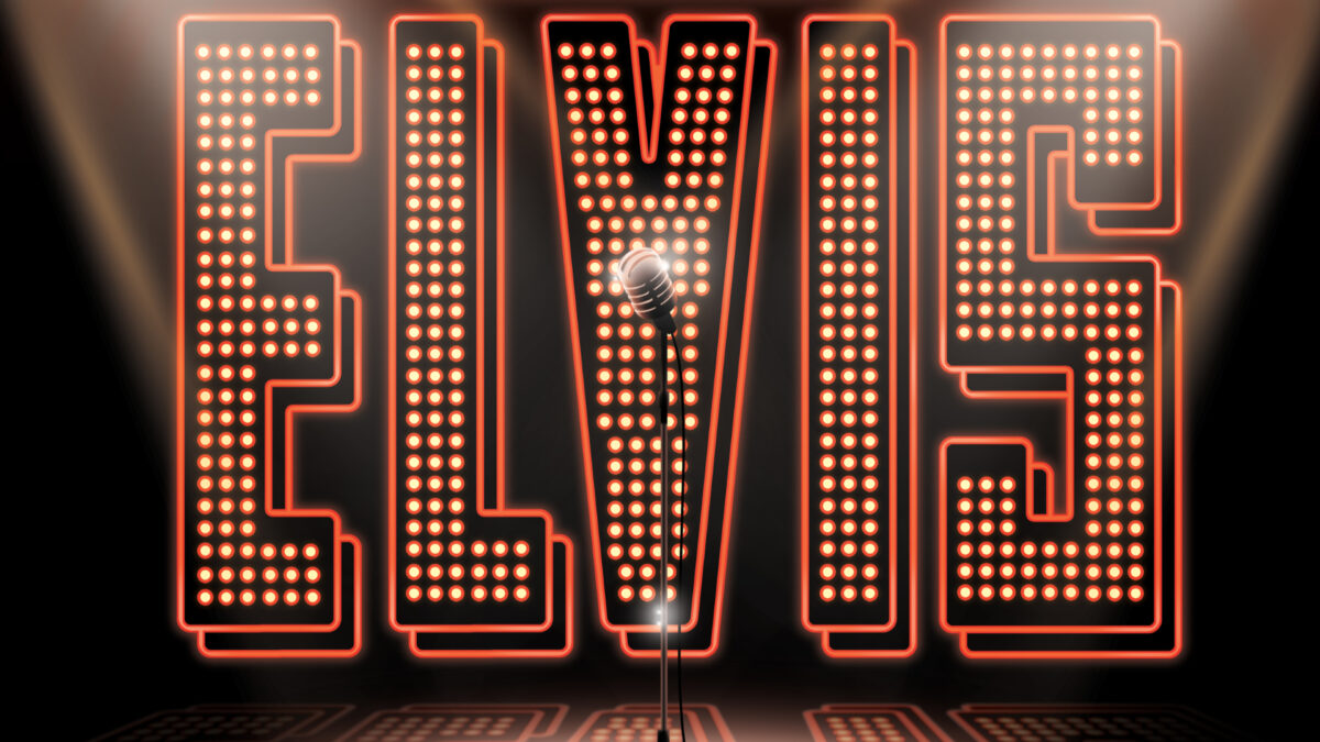 A radiant Elvis lettering with a microphone stand in front of it in the spotlight.