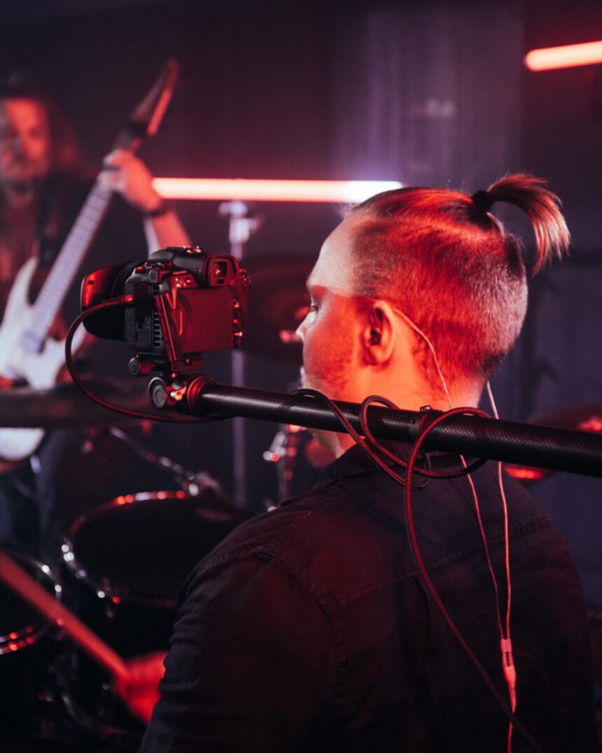 A camera, attached to a telescope, is held over the shoulder of a drummer.