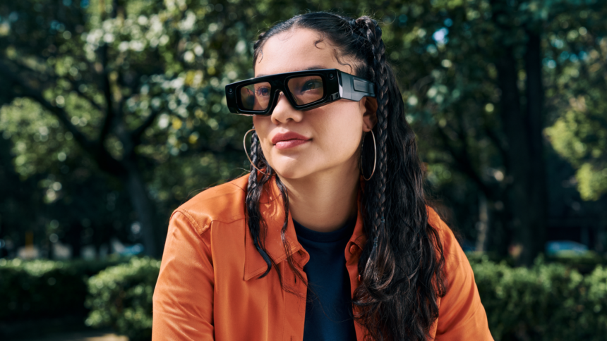 A woman sits in the park wearing Snap's Spectacles AR headset.