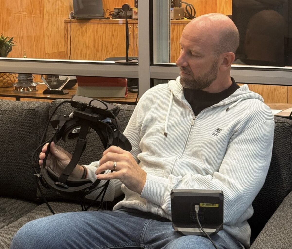 Bosworth sits on a couch and looks at the wide-fov prototype of a VR headset.