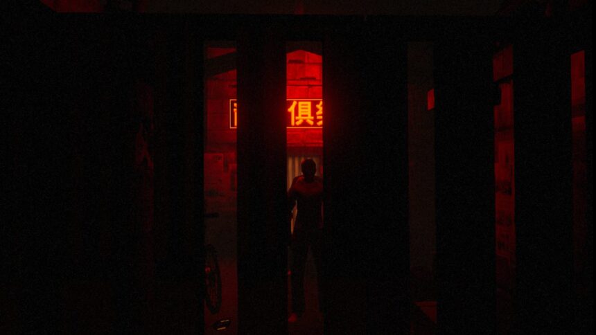 The silhouette of a man can be seen behind wide bars in red neon light.